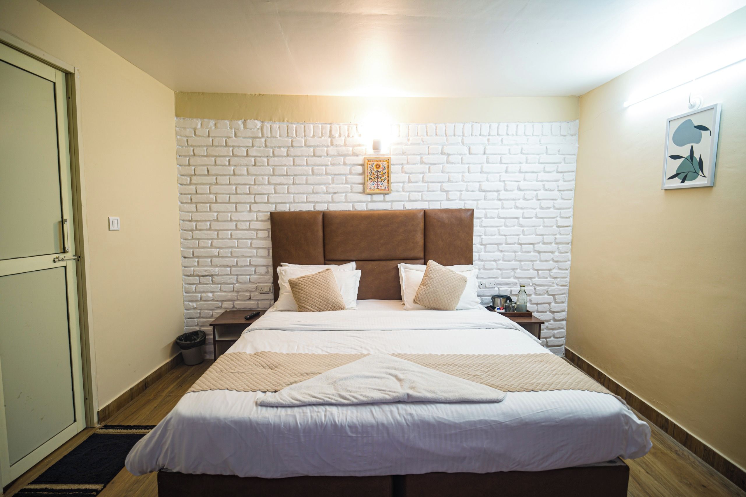 A hotel room with a white brick wall, a brown headboard, and a bed with white bedding.
