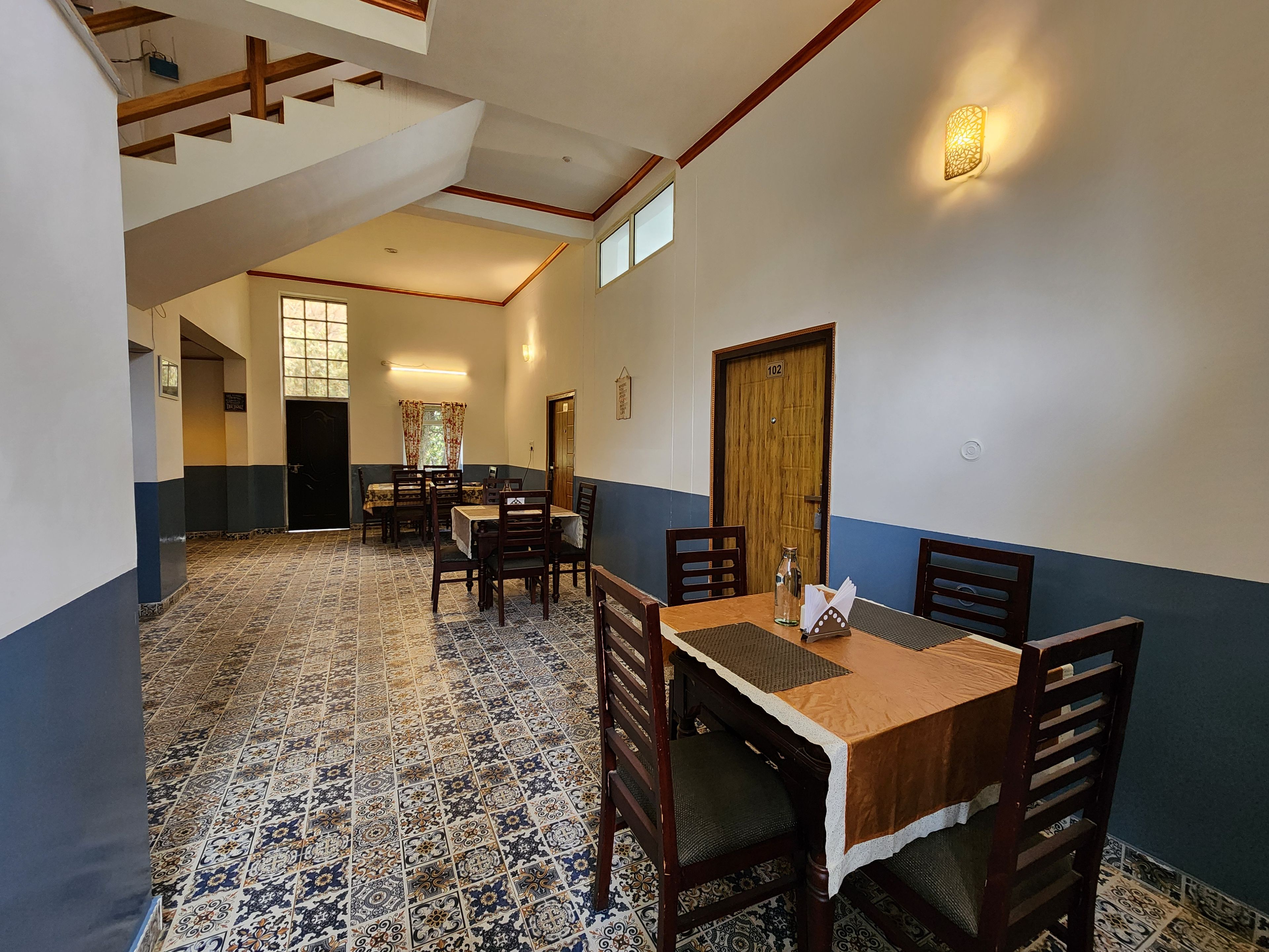 A dining area with a high ceiling, patterned floor tiles, and a staircase.