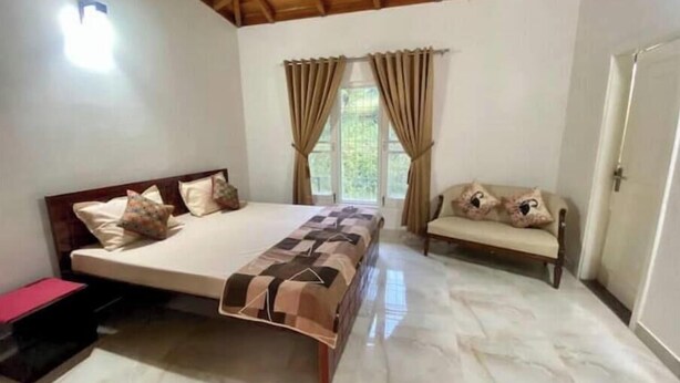Ein Schlafzimmer mit Holzboden, einem Bett mit gemustertem Überwurf, einer Bank mit Kissen und einer Tür.