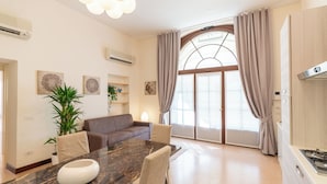 Ein modernes Wohnzimmer mit Esstisch, Sofa und einem großen Fenster mit Vorhängen.