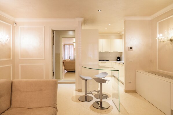 A modern kitchen with white cabinets, a glass bar counter, and two bar stools. - Residenza Lugo (Verona)
