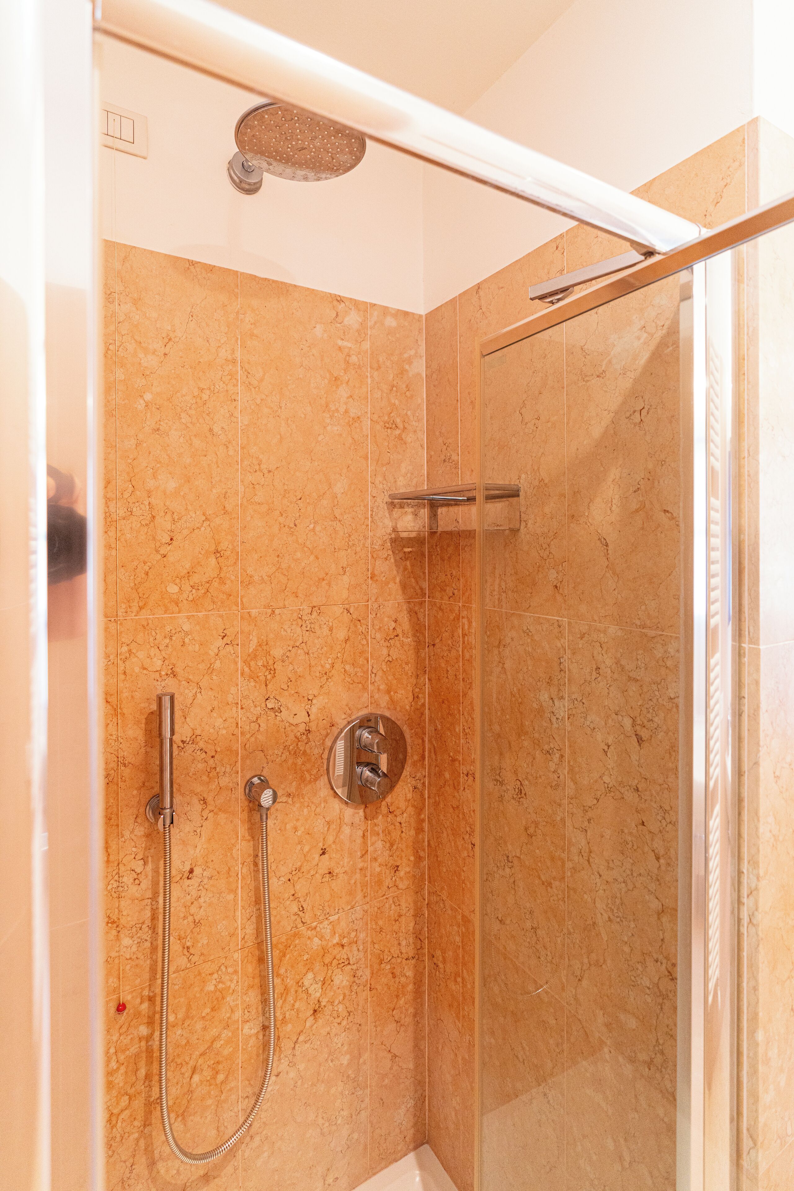 A glass-enclosed shower with a handheld showerhead and a wall-mounted faucet.