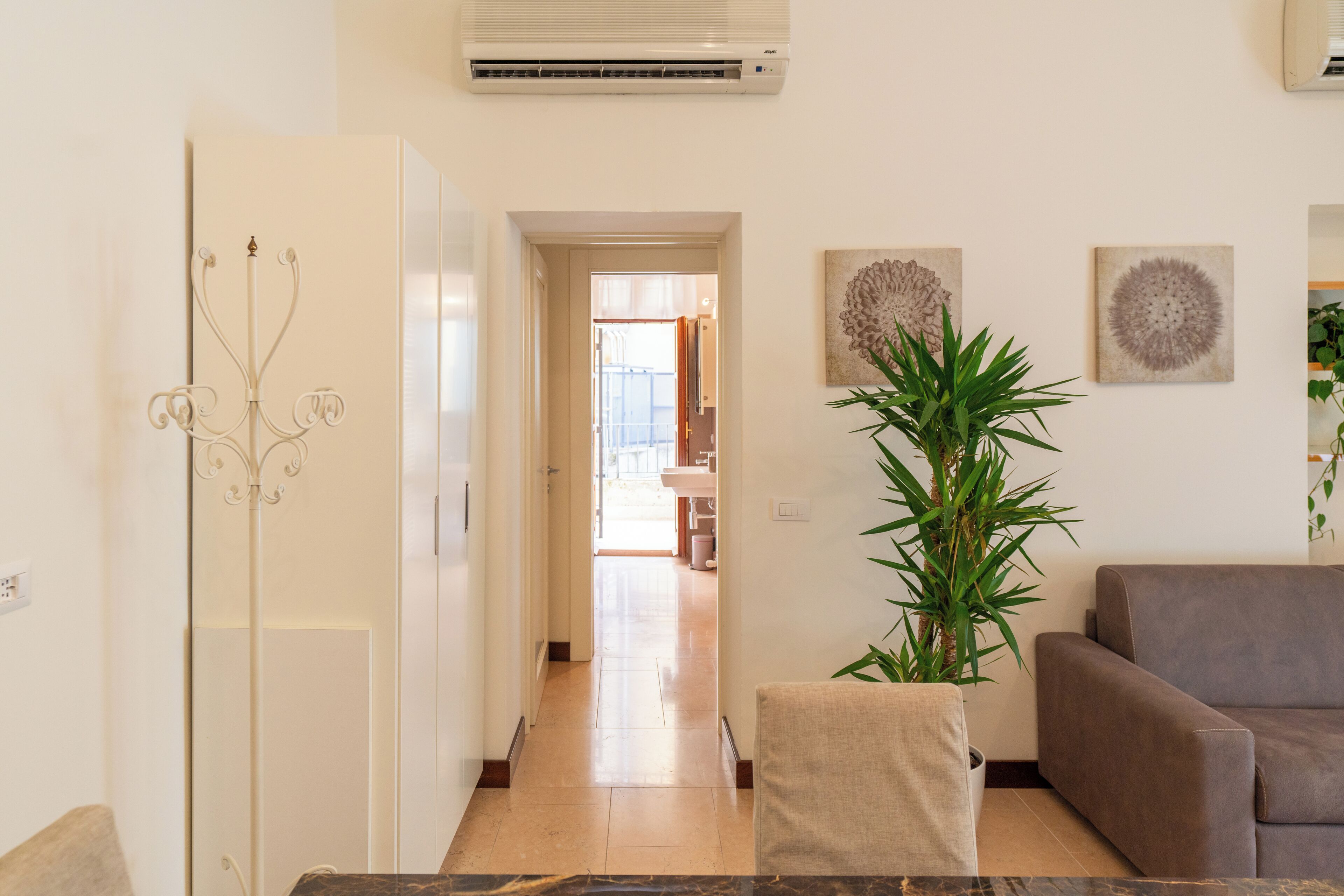 A hallway leading to a bathroom with a white door, a potted plant, and a brown couch.