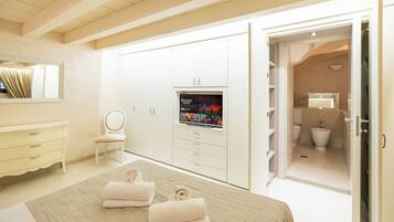 Une chambre avec un lit, un téléviseur posé sur un meuble, une armoire, une salle de bain visible à travers une porte ouverte, et une chaise.