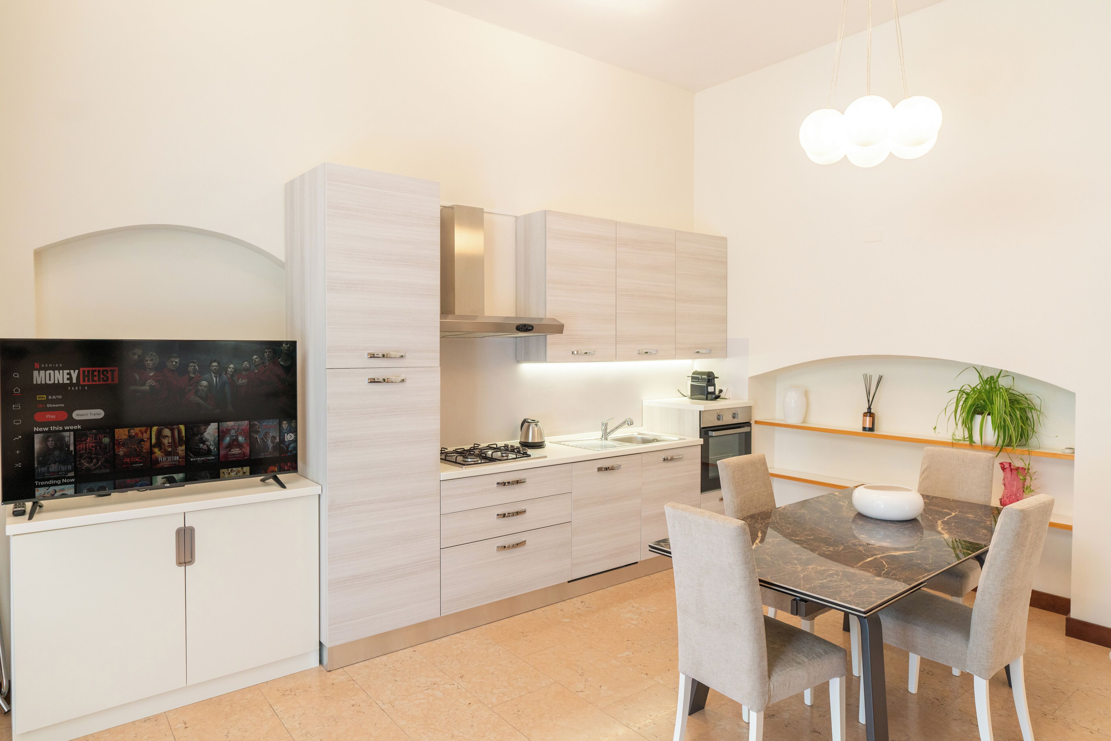 A modern kitchen with a built-in stove, a dining table with chairs, and a TV mounted on the wall.