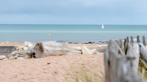 Una playa con una cerca de madera, un velero a lo lejos y un cielo despejado.