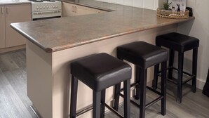 Een moderne keuken met een centraal eiland, barkrukken, een inbouwoven en een witte betegelde achterwand.