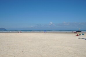 Una extensa playa de arena con algunas sombrillas y sillas, una montaña distante, y el océano.