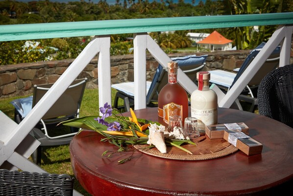 A table with a bottle of wine, a glass, and some food items on a wicker chair outdoors. - Villa La Louisiane (Deshaies)