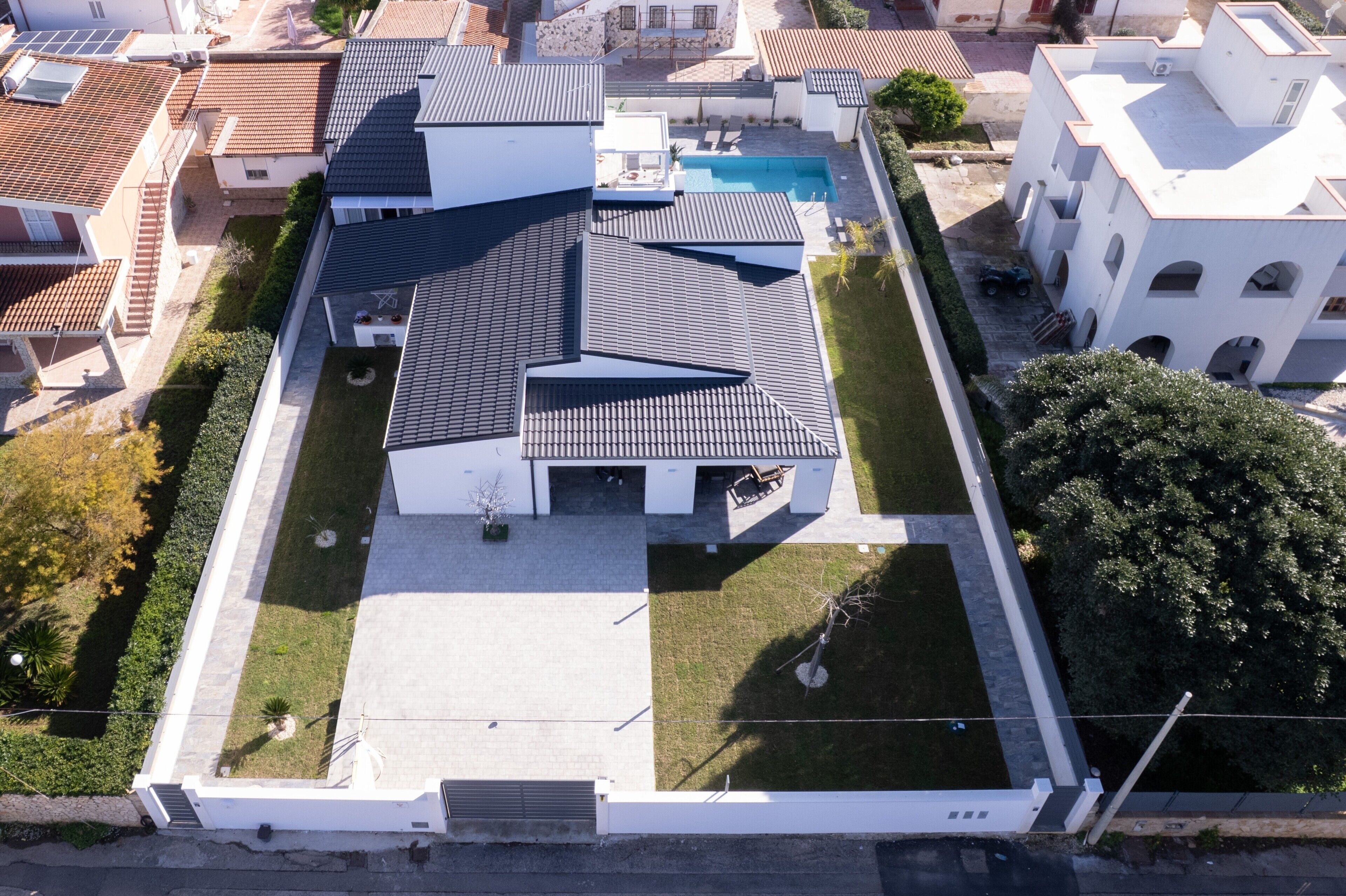 An aerial view of a modern building with a flat roof, a swimming pool, and a well-maintained lawn.