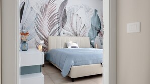 A bedroom with a bed, nightstands, a wall art piece, and a vase with flowers.