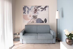 Ein modernes Wohnzimmer mit einem grauen Sofa, einem runden Beistelltisch, einer Stehlampe und einem floralen Kunstwerk an der Wand.