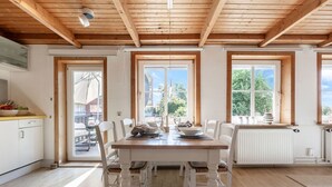 A dining area with a wooden table, white chairs, and large windows. - HUUS BADSTAVEN – Holiday Apartment Leuchtturm in Burg's Most Beautiful Alley (Fehmarn)