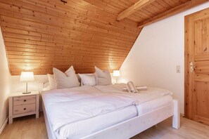 Une chambre avec un plafond en bois, un lit avec une literie blanche, deux tables de chevet avec des lampes et une armoire en bois.