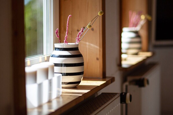 Une fenêtre avec un vase rayé contenant des fleurs roses et un chandelier.