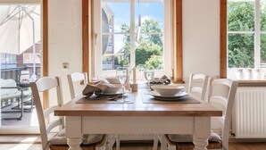 A dining area with a wooden table, white chairs, and a view of the outside. - HUUS BADSTAVEN – Holiday Apartment Leuchtturm in Burg's Most Beautiful Alley (Fehmarn)