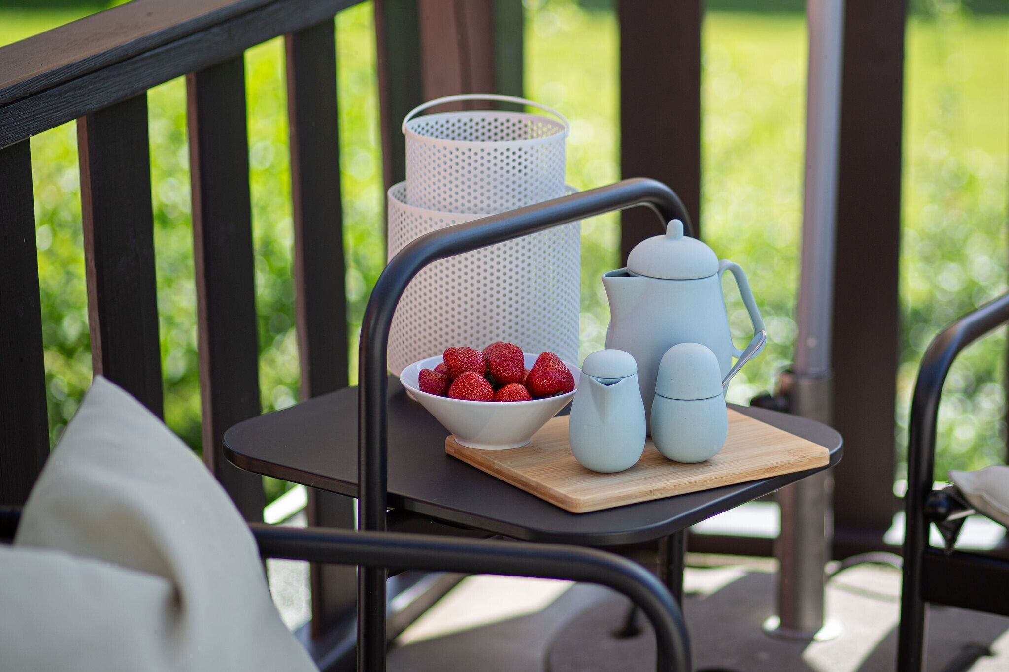 A table with a bowl of strawberries, a white mesh container, and two white pitchers on a wooden tray.