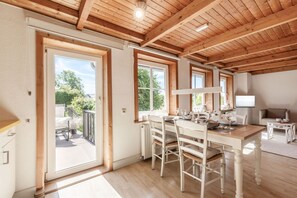 Una habitación amplia con techo de madera, un comedor con mesa y sillas, y vistas al exterior a través de amplios ventanales.