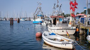 A marina with boats docked, including a white boat with 'NIMMERSAATT' and a smaller boat with 'BURGSTAAKEN' on it. - HUUS BADSTAVEN – Holiday Apartment Leuchtturm in Burg's Most Beautiful Alley (Fehmarn)