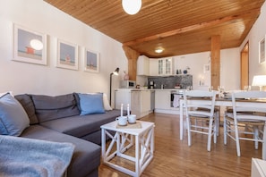 Una sala de estar moderna con un sofá gris, una pequeña mesa blanca con velas y un comedor con sillas blancas y una mesa.