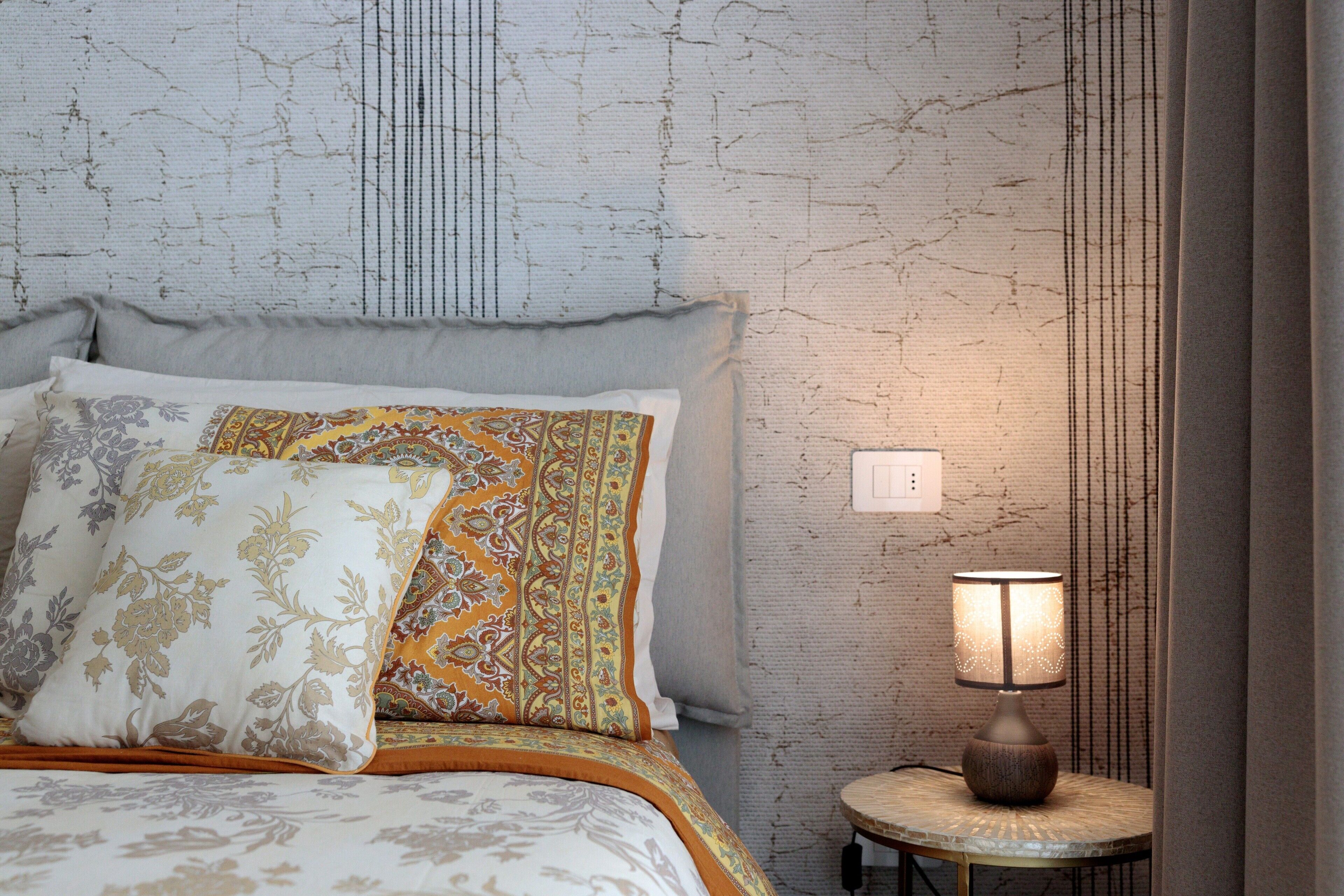 Een bed met beddengoed met patroon, een bedlampje en een gestructureerde muur.