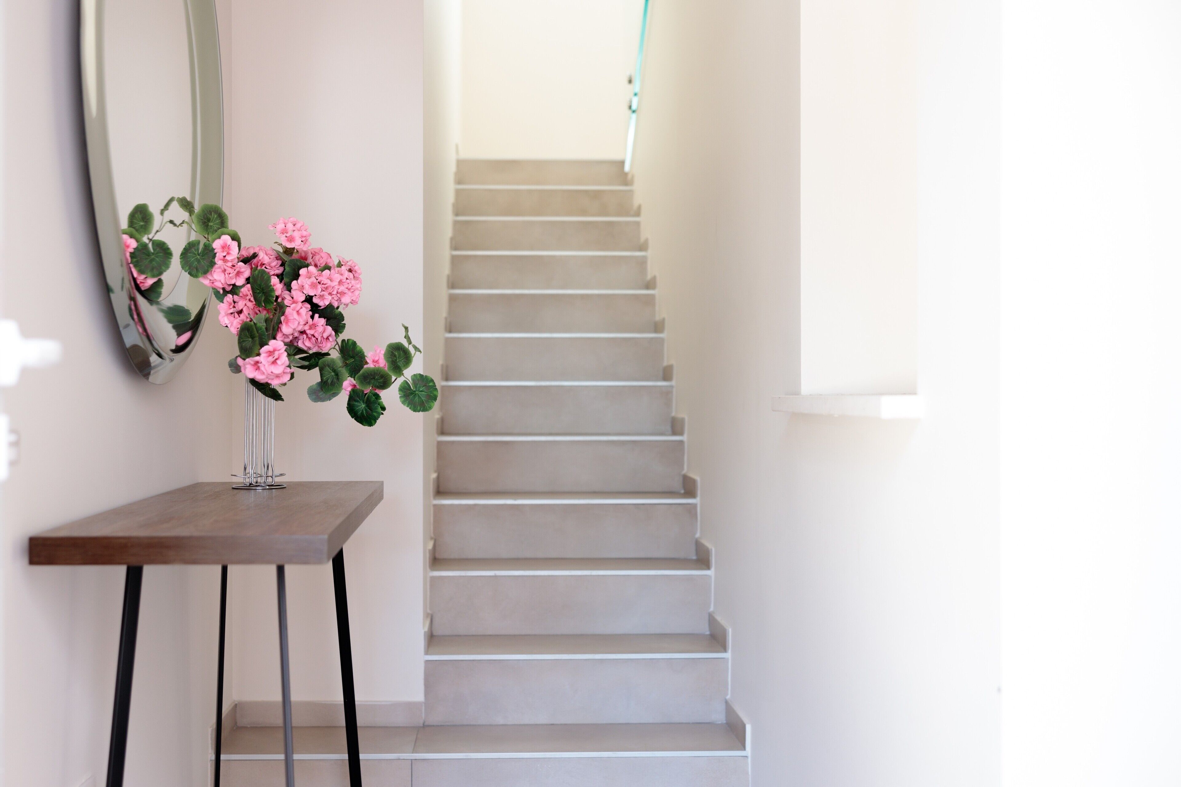 A staircase with a vase of pink flowers on a wooden table.