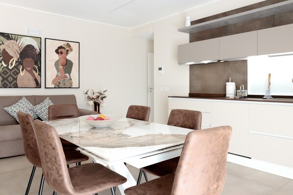 A modern dining area with a marble table, cushioned chairs, a bowl of fruit, and artwork on the wall.