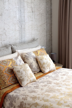 A neatly made bed with floral patterned bedding, a headboard with a textured design, and a bedside lamp.