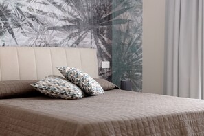 A bed with a quilted cover, two patterned pillows, and a wall with a leaf pattern. - Apartment 'Athena' with Shared Pool, Wi-Fi and Air Conditioning (Fontane Bianche)