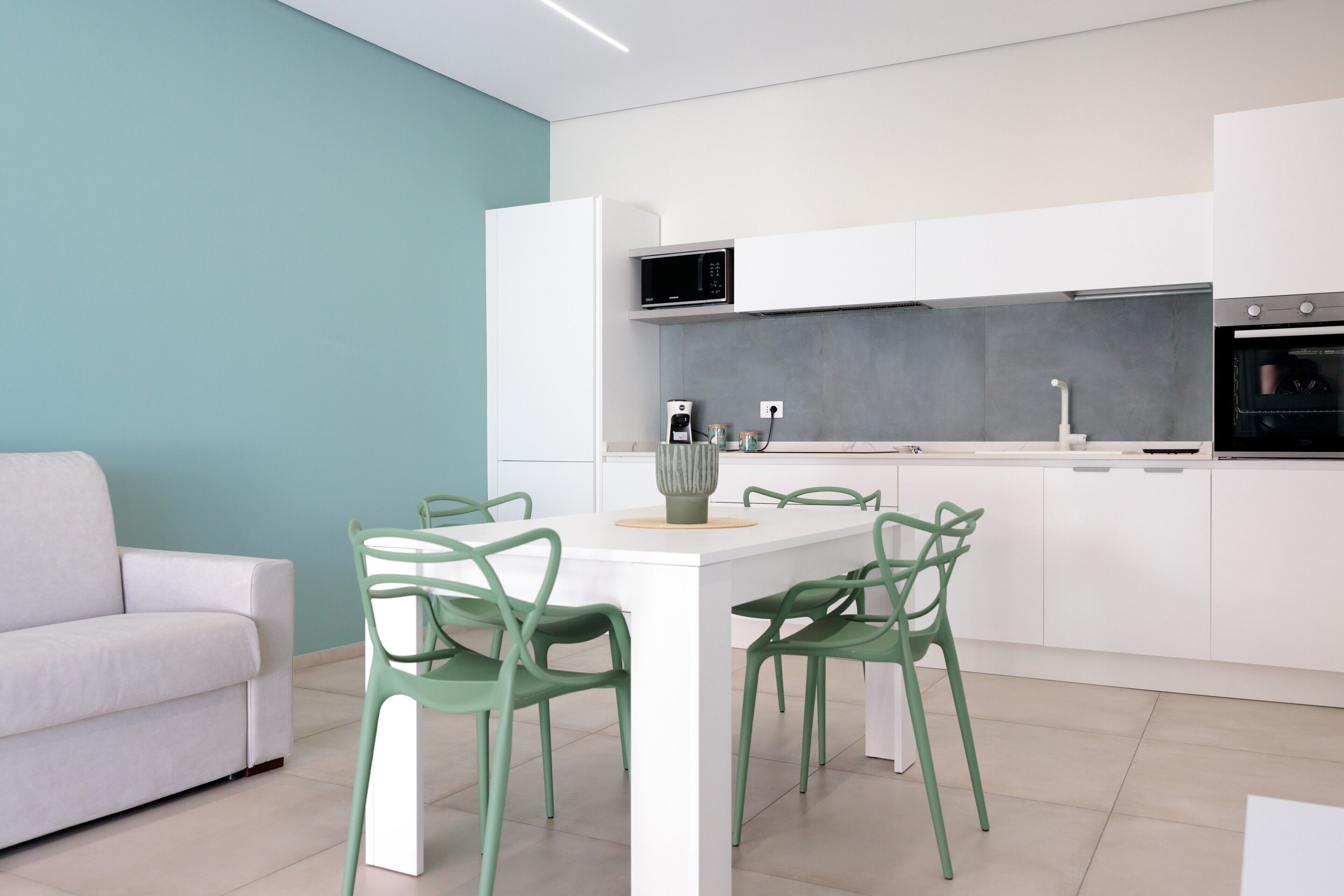 Une cuisine moderne avec des meubles blancs, un four à micro-ondes encastré et un coin repas comprenant une table blanche et des chaises vertes.
