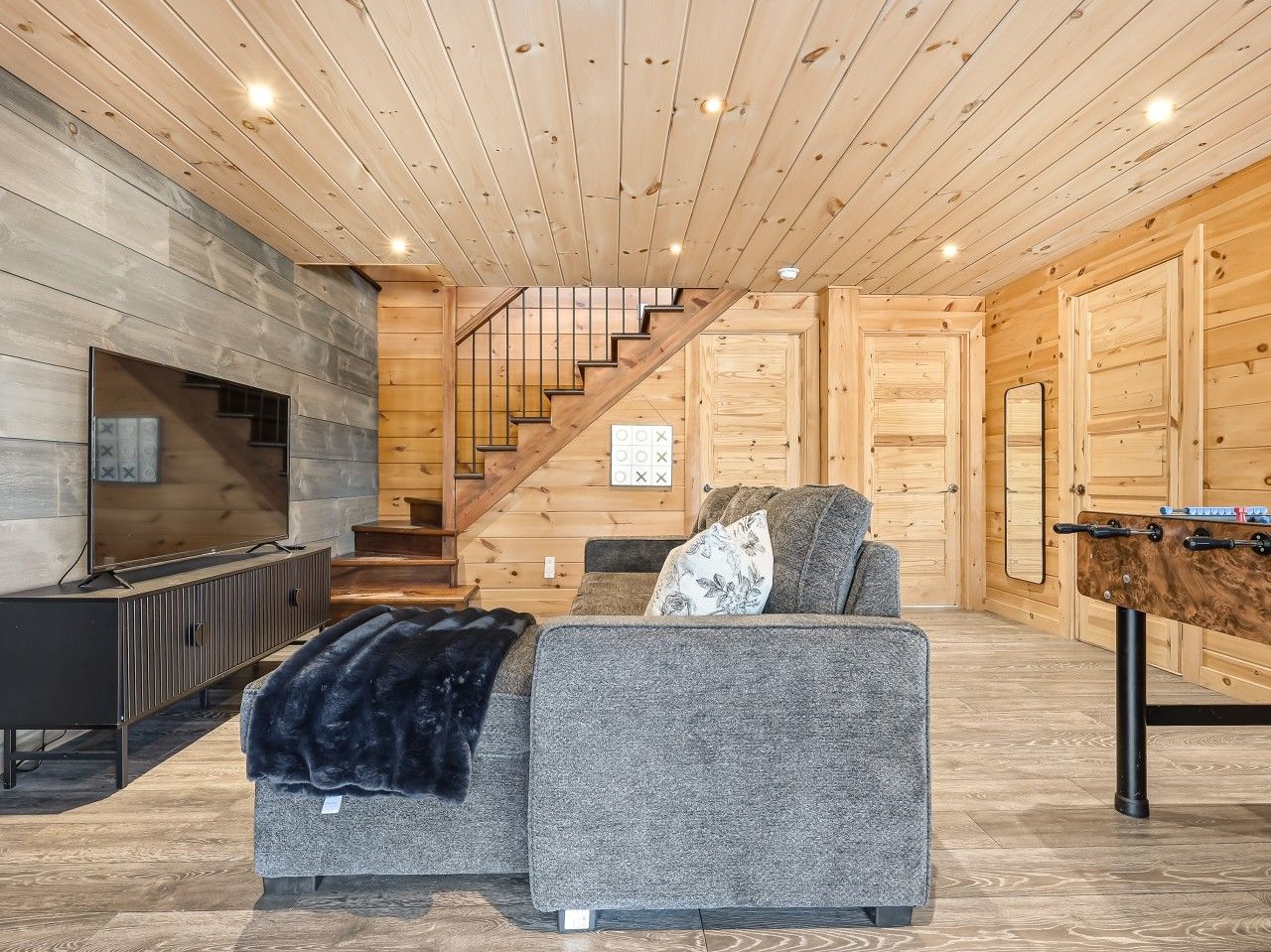 A modern interior with a sofa, a flat-screen TV, a staircase, and a foosball table.