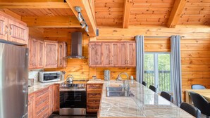 A log cabin kitchen with wooden cabinets, a stainless steel refrigerator, a microwave, a stove, and a sink. - Henö - Entre lac & forêt (Mandeville)