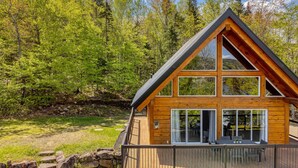 A wooden cabin with a triangular roof, large windows, and a deck area. - Henö - Entre lac & forêt (Mandeville)
