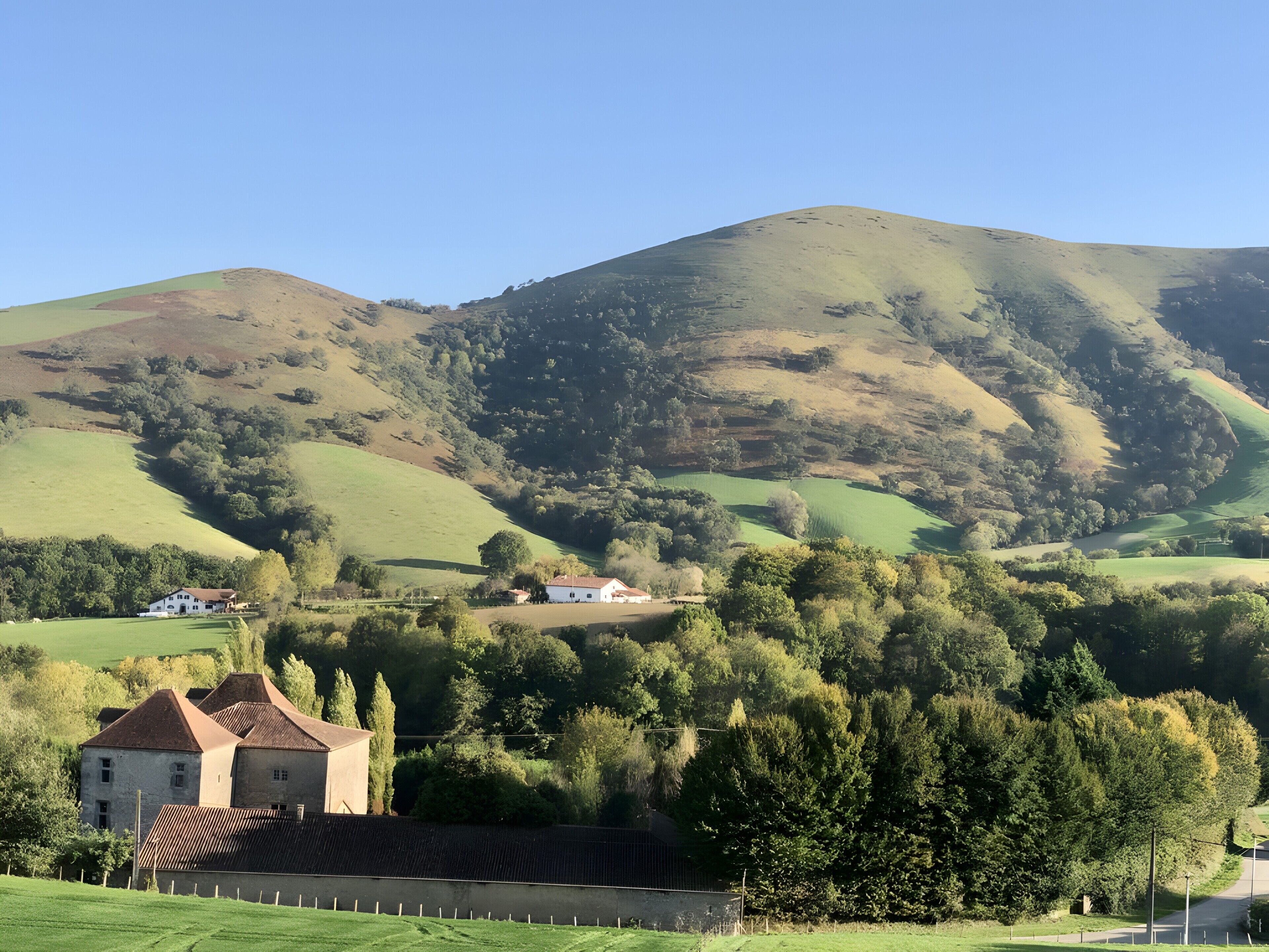 Un paysage rural avec des collines ondoyantes, un bâtiment blanc avec un toit rouge et une clôture.