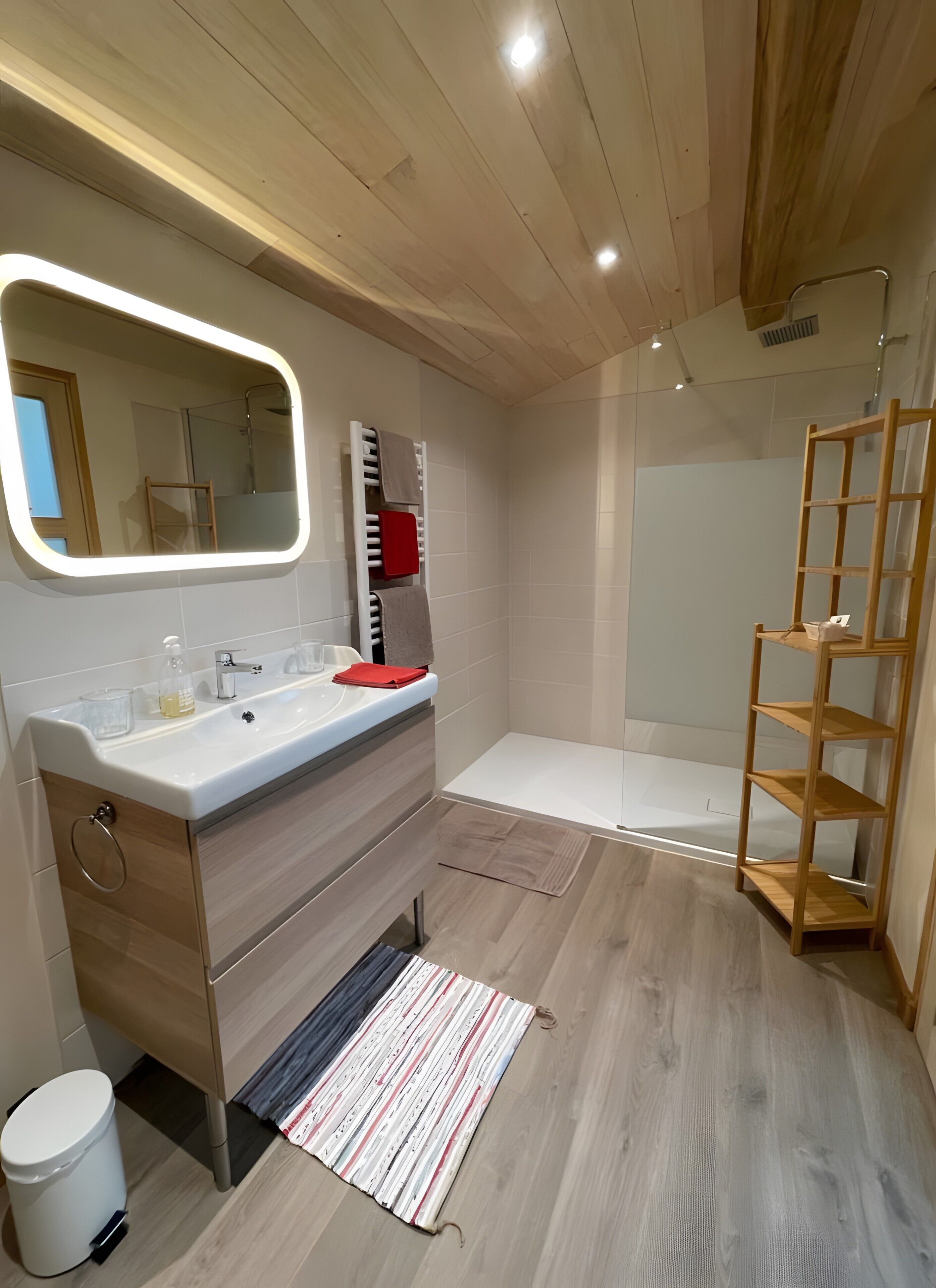 Ein modernes Badezimmer mit Waschtisch, Spiegel, Dusche und einem Holzboden.