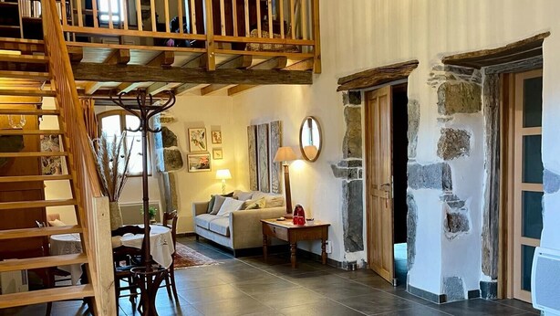 A spacious loft-style room with a wooden staircase, a cozy sofa, a dining table, and a stone wall. - Guest Room 'Olceiry' with Mountain View, Private Garden and Wi-Fi (Iholdy)