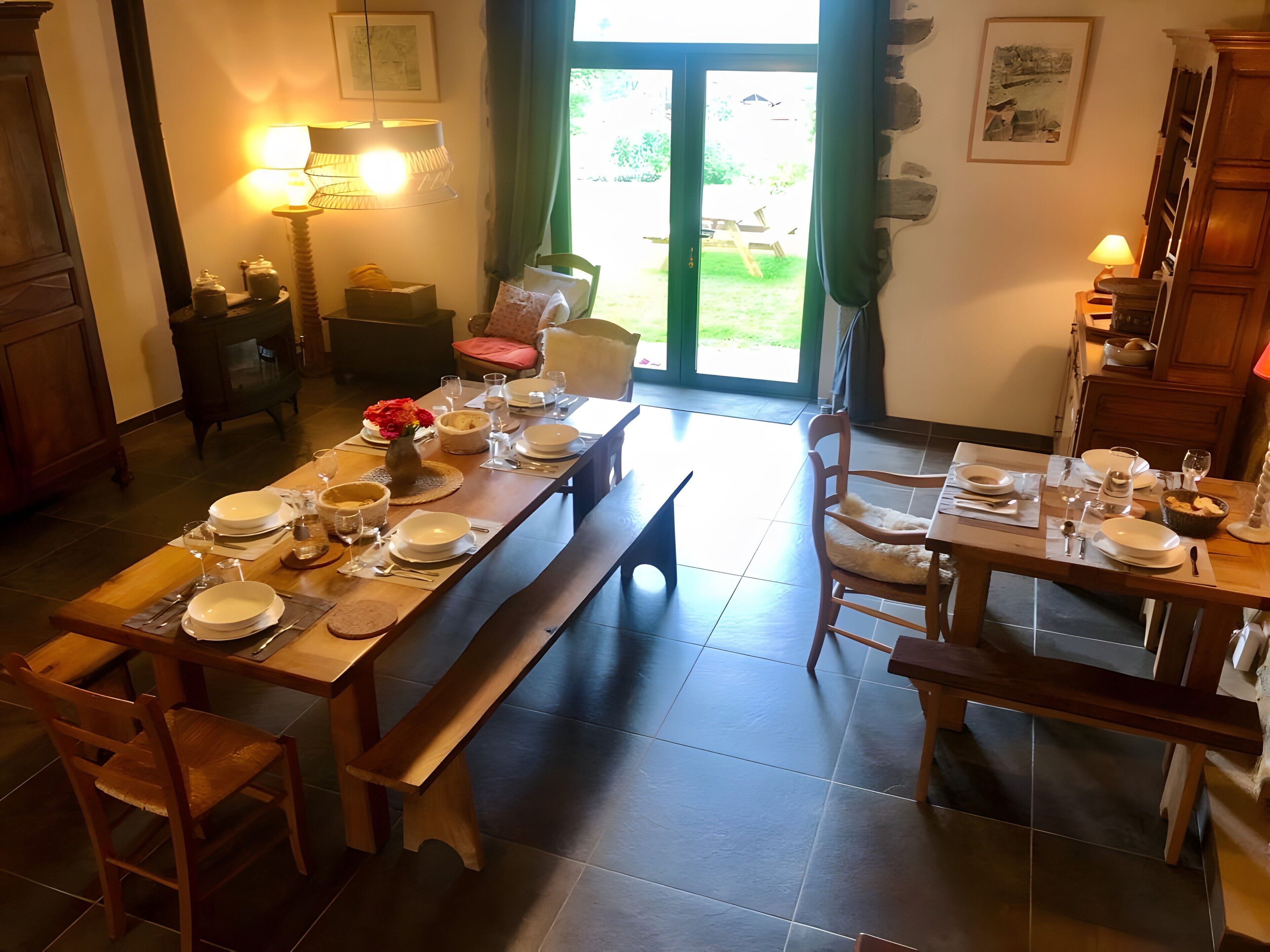 Een eetruimte met een lange tafel gedekt voor een maaltijd, stoelen, een bank en uitzicht op de omgeving door een glazen deur.