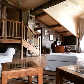 A rustic interior with a wooden staircase, a sofa, a coffee table, and a fireplace.