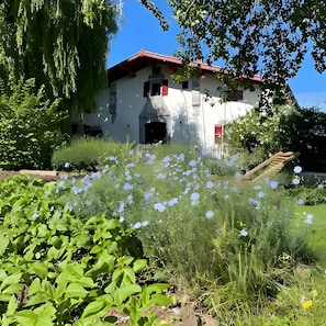 A building with a red roof, surrounded by greenery and white flowers.