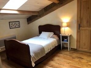 Un dormitorio con una cama de madera, una mesita de noche con lámpara, una puerta y una pared con un cuadro enmarcado.
