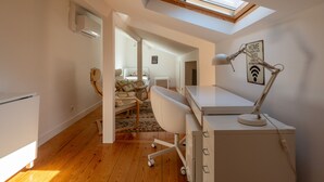 Un dormitorio pequeño con un tragaluz, un escritorio con lámpara, y una cama con vista a otra habitación.