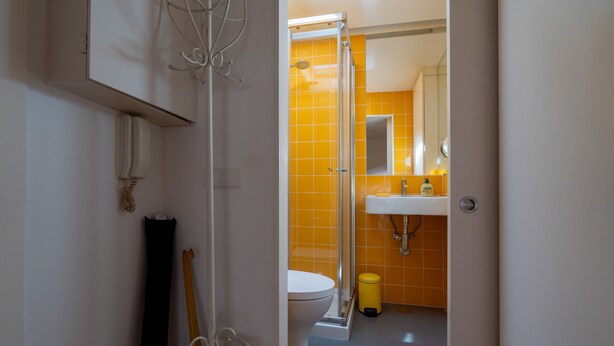 A bathroom with a yellow-tiled shower, a white toilet, and a sink with a mirror above it. - Bairro Alto Tiny Studio by Homing (Lisbon)