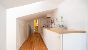 Una cocina estrecha con suelo de madera, armarios blancos y una pequeña isla con un lavamanos.