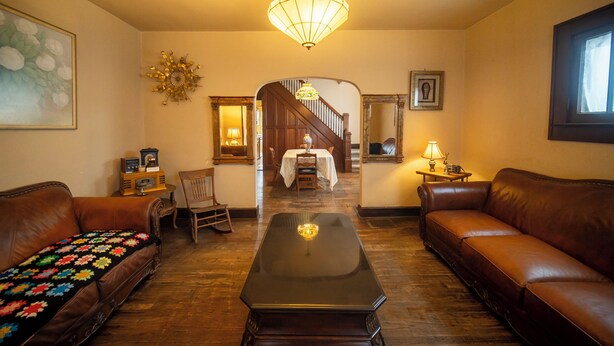 Una sala de estar con un sofá de cuero marrón, una mesa de centro negra y piso de madera. Se ve una escalera que sube a otra habitación.