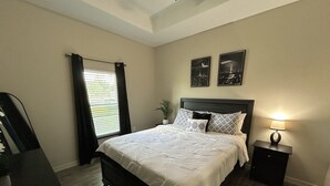A bedroom with a bed, a nightstand, a lamp, a window with curtains, and two wall-mounted pictures.