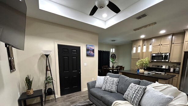A modern living room with a grey sofa, black and white patterned pillows, and a black and white rug. There is a dining area with a table and chairs, and a kitchen with a microwave and stove.