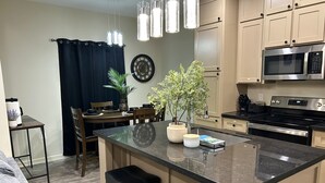 A modern kitchen with a central island, stainless steel appliances, and a dining area with a dark curtain.