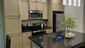 A kitchen with beige cabinets, a black countertop, stainless steel appliances, and a potted plant.