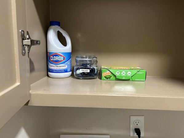 Estante con una botella de lavandina Clorox, un tarro con cápsulas Tide y una caja de detergente para ropa Gain original.