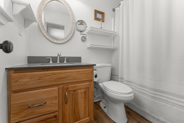 A bathroom with a wooden vanity, a round mirror, a toilet, and a shower curtain.